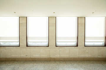 A corridor in a building with four windows on a beige tile wall.