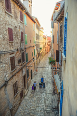 Two tourists packed with suitcases arriving in Rovinj Old Town trough the narrow street during noon on a sunny day captured in a vertical shot
