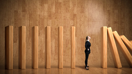 businesswoman as a stopper between falling domino-blocks on wooden background