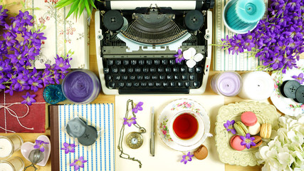 Romantic vintage overcrowded writer's desk creative composition with old fashioned typewriter, books, flowers and feminine clutter.