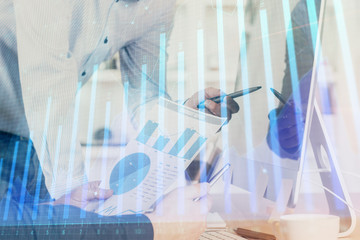 Double exposure of chart with businessman typing on computer in office on background. Concept of...