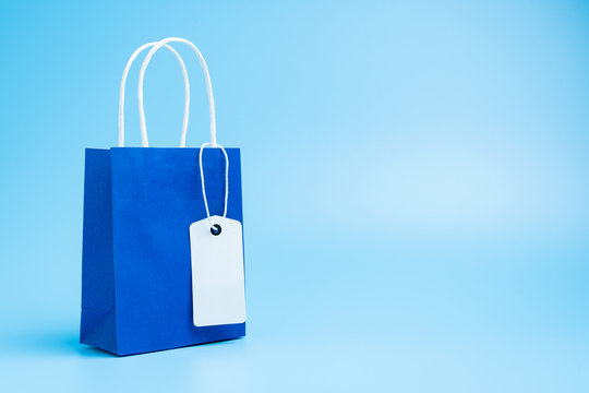 Single blue shopping or gift bag with blank label tag isolated on blue background