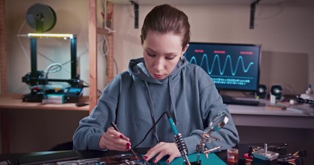 Woman electronics engineer is soldering an electric board in her workshop. Girl student are studying electronics and soldering in classroom.