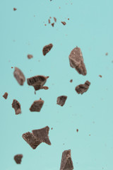 Falling pieces of dark chocolate on a light blue background, freezing in motion