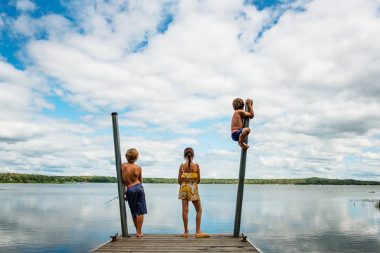 Rear view of Three children in swimwear standing on a dock fishing and messing about on a summer day, USA