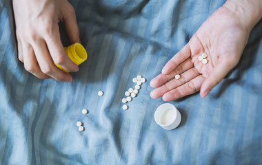 Hand close-up image with a large number of pills scattered on the quilt 