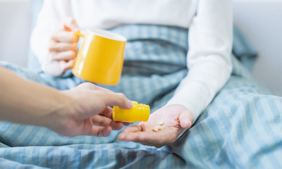 A hand giving pills to patient lying on the bed 