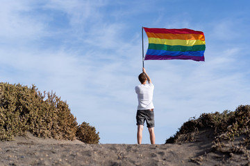 A man holds an LGBT flag developing in the wind against a blue sky. Rainbow. Symbol of same-sex relationships.