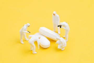 Miniature people doctors with protective suit and mask research on white pills tablet medicine on yellow background, Corona virus, COVID-19 flu medicine or virus vaccine medical research concept