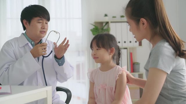 Smiling asian man doctor pediatrician holding stethoscope examining listening kid girl checking up preschool patient visit pediatrician with mom