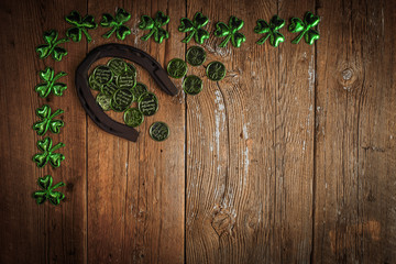 Background with rusty horseshoe and clover leaves and coins over rustic wood.