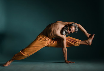 Old man with grey beard doing yoga, pilates, fitness training, stretching exercise, asana or balance workout on floor