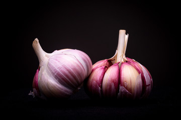 Closed and peeled skin purple garlic lots next to each other in studio with dramatic light against a dark background