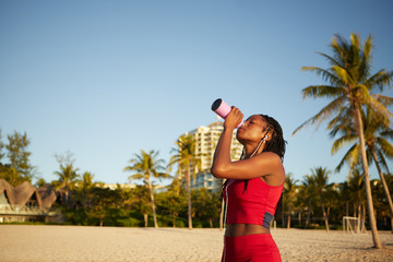 Fit slim woman drinking water after running on the beach on the morning