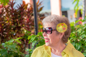 A senior woman at a restaurant in Hawaii, with a cute tropical drink umbrella in her hair. She...