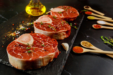Raw beef shank and spices for preparing ossobuco dish on black background.