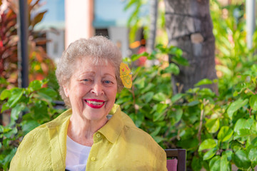 A senior woman at a restaurant in Hawaii, with a cute tropical drink umbrella in her hair. - obrazy, fototapety, plakaty
