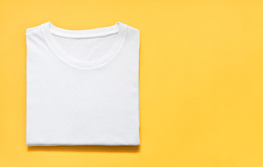 top view of folded white color t-shirt on yellow background, copy space, flat lay