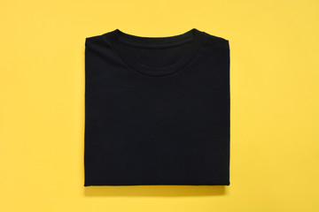top view of folded black color t-shirt on yellow background, copy space, flat lay