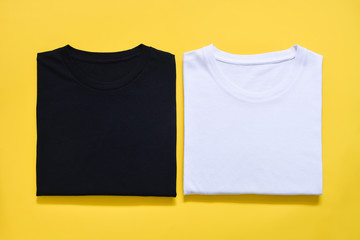 top view of folded black and white color t-shirt on yellow background, copy space, flat lay