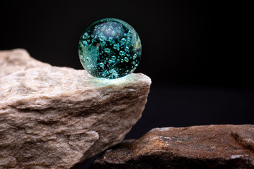 Vibrant teal green glass marble shining its light on reflecting textured surface of a white stone...