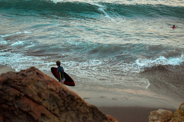 Hombre camina y observa las olas mientras sostiene su tabla de surf