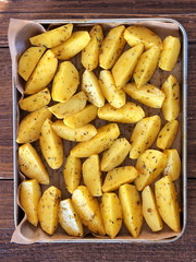 Raw potato wedges in oil and herbs for baking, close-up.