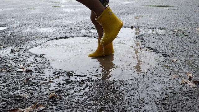 slow motion kid wearing yellow boot playing water rain puddle on road