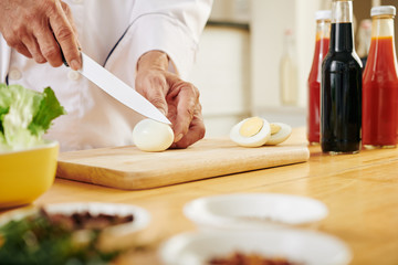 Hands of chef cutting boiled chicken eggs when cooking salad at kitchen