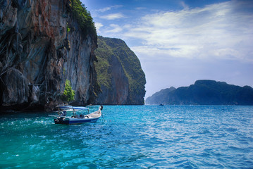 Boat on crystal clear water on a sunny day near rocks in Phuket, Thailand