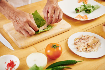 Hands of man wrapping pieces of chicken fillet in lettuce leaves when cooking healthy appetizers