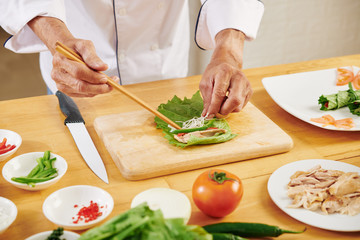 Hands of man making lettuce rolls with chicken, shredded cheese and bell pepper