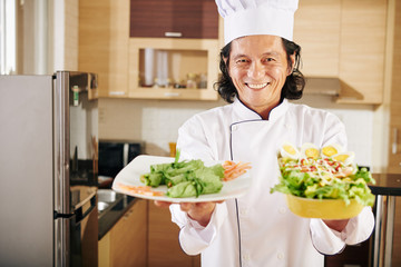Portrait of happy smiling man showing plates with appetizers and salad he cooked for dinner