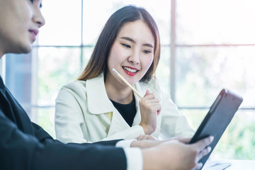 Smiling Asian business woman hold pencil in hand while listening to suggestions from manager. Smart coworkers discuss, brainstorm for operating performance report. Communication and business concept