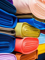 Rolls of bright multicolored fabric close-up. Many different fabrics are rolled up and lying on the shelves. Samples of different natural fabrics in the warehouse of the fabric factory