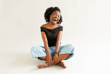 Laughing young woman sitting on the floor posing with legs crossed on white background