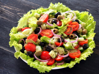  Raw vegetable salad - lettuce, onion, tomato, cucumber, olives on a rustic wooden table.
