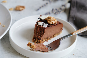 Piece of homemade chocolate raw vegan cake - healthy dessert made from coconut milk, butter, cashew, cacao, walnut