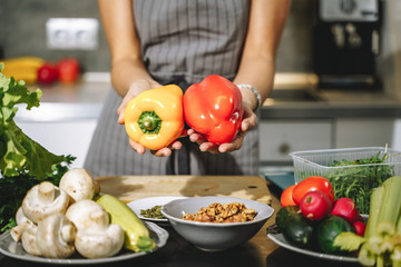 Close up of female hands holding fresh yellow and red peppers in their hands in the kitchen.