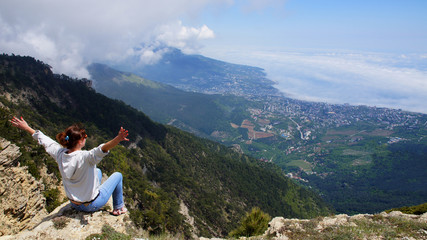 A young girl sits on top of a mountain with arms outstretched.