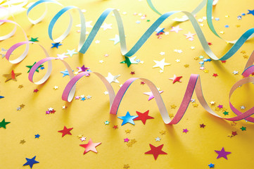 Colorful carnival serpentines and party confetti stars on yellow background.
