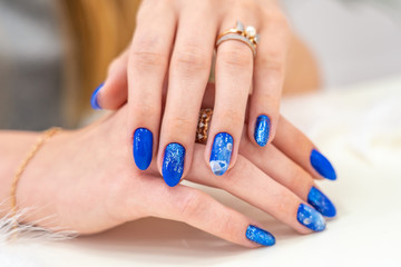 Obraz na płótnie Canvas Hands of a girl with a beautiful blue manicure are on display. blue glossy nail