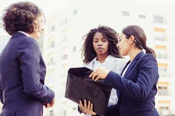 Cheerful employees discussing papers outdoor. Cropped shot of young multiethnic businesswomen standing with briefcase on street. Business concept