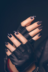 Hands of girl with black manicure in black leather gloves with cropped fingers.