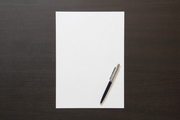 Template of white paper with pen on dark wenge color wooden background.
