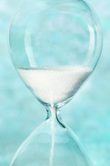 Time concept. An hourglass close-up on an abstract background, with sand leaking through. Blue toned image