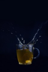 Splash. Plop. Tea and falling sugar cube.Cup of tea against blue background. Tea splash isolated on blue backdrop.