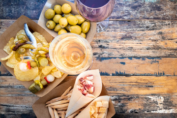 Tapas, pinchos, and wine. Cheese, jamon and olives, spicy gildas and potato chips, shot from the top on a wooden table in an outdoors cafe with a place for text