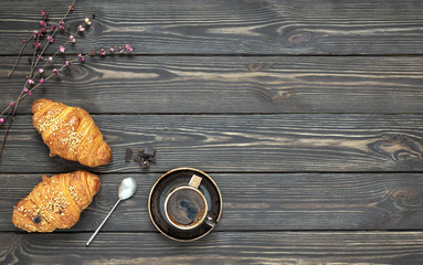 Breakfast scene, fresh croissants and a cup of espresso. Bouquet of spring flowers on the table. Dark wooden background. Top view.