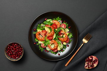 Shrimps salad with cherry tomatoes, cucumeber, avocado, lettuce and pomegranate on dish. Healthy seafood concept. Tasty grilled prawn shrimp and mix vegetable salad on black, top view.